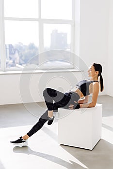 Young woman sitting on a box at gym after her workout. Female athlete taking rest after exercising at gym