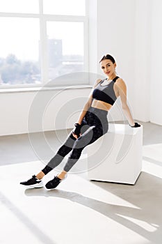 Young woman sitting on a box at gym after her workout. Female athlete taking rest after exercising at gym