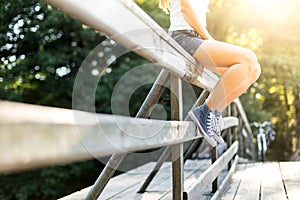 Young woman sitting on a bridge railing in jeans sneakers