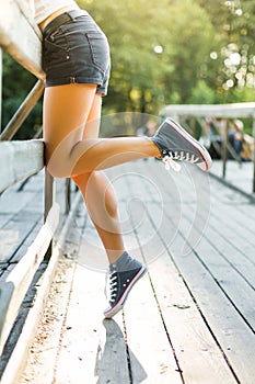 Young woman sitting on a bridge railing in jeans sneakers