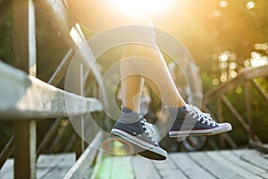 Young woman sitting on a bridge railing in jeans sneakers