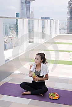 Young woman sitting on a building rooftop terrace, taking a break from a hard workout and drinking water