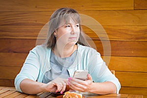 A young woman sitting in cafe near wooden table with mobile phone and a cup of coffee