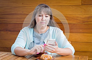 A young woman sitting in cafe near wooden table with mobile phone and a cup of coffee