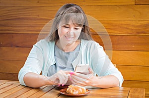 A young woman sitting in cafe near wooden table with mobile phone and a cup of coffee