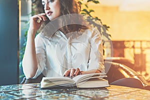 Young woman sitting in cafe at table with a paper book. Girl waiting for friends in restaurant and reading book