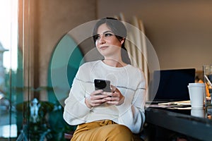 Young woman sitting cafe at table, thoughtfully looking out window, holding smartphone.Portrait girl with cell phone in her hands