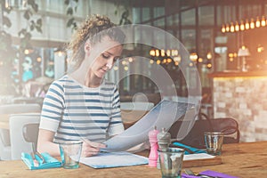 Young woman is sitting in cafe at wooden table and reading. Girl is waiting for friends,colleagues in restaurant.