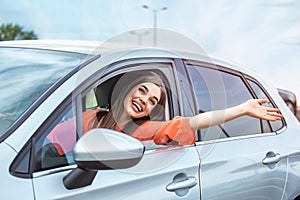 Young woman sitting in a car hand out of window. Happy woman driving a car and smiling. Portrait of happy female driver steering