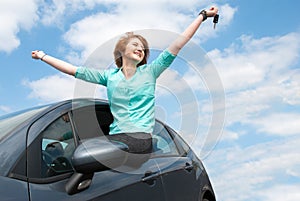 Young woman sitting in the car and holding a key against blue sk