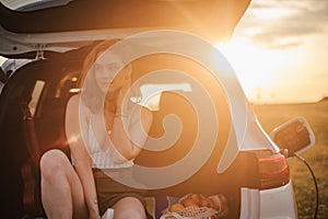 Young woman sitting in a car trunk, waiting for charging.