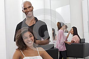 Young woman sitting on chair with hairstylist standing behind photo