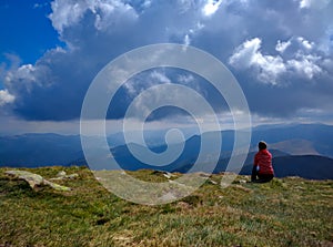 Young woman sitting on a cliff looking at mountains view and blue cloudy sky. Young girl dreaming about traveling