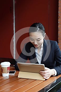 Young woman sitting in coffee shop at wooden table, drinking coffee and using pad.On table is laptop