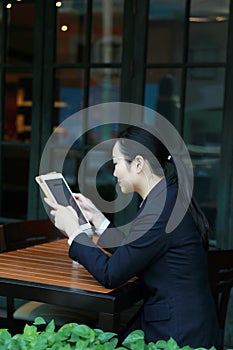 Young woman sitting in coffee shop at wooden table, drinking coffee and using pad.On table is laptop