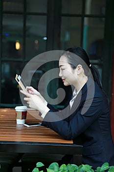 Young woman sitting in coffee shop at wooden table, drinking coffee and using pad.On table is laptop