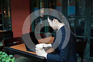 Young woman sitting in coffee shop at wooden table, drinking coffee and using smartphone.On table is laptop