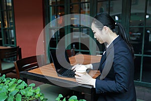 Young woman sitting in coffee shop at wooden table, drinking coffee and using smartphone.On table is laptop