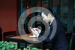 Young woman sitting in coffee shop at wooden table, drinking coffee and using smartphone.On table is laptop