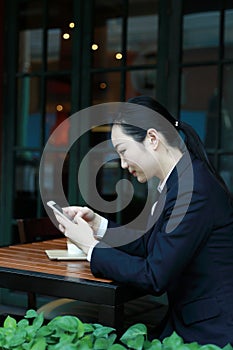 Young woman sitting in coffee shop at wooden table, drinking coffee and using smartphone. On table is laptop