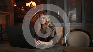 Young woman sitting in coffee shop at wooden table, drinking coffee and using smartphone.On table is laptop. Girl