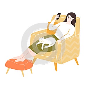 Young woman sitting in comfy yellow chair with footrest, using smartphone. Stay home concept. Girl with a white cat