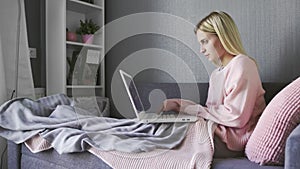 Young woman sitting on couch using laptop notebook looking at screen typing message