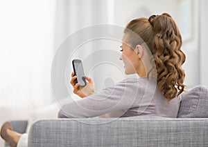 Young woman sitting on couch and writing sms