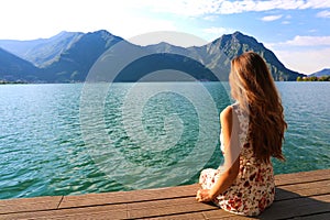 Young woman sitting on a deck by the water, looking into the distance. Carefree bright future concept. Back view beautiful woman
