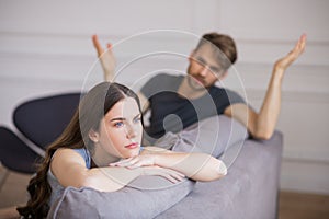 Young woman sitting with a depressed look while her husband blaming her