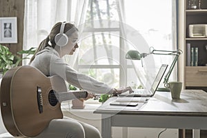 Woman playing guitar and connecting with her laptop