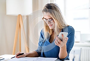 Young woman sitting at the desk indoors in home office, working.