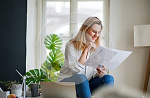 Young woman sitting on desk indoors in home office, working.