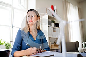 Young woman sitting at the desk indoors in home office, working.