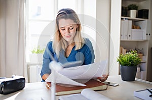 Young woman sitting at the desk indoors in home office, working.