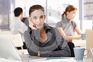 Young woman sitting at desk others working behind