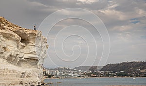 Young woman sitting at the edge of a cliff enjoying the sea scenery. Pissouri coastline Limassol Cyprus