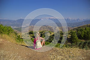 Young woman sitting at edge of cliff looking over expansive view of plains and mountains