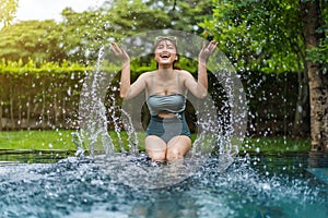 Woman sitting on edge of swimming pool and playing water splashing