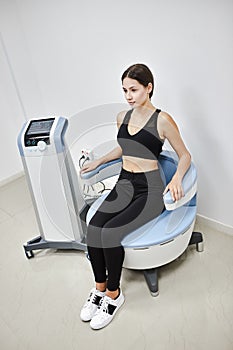 Young woman sitting on electromagnetic chair for stimulation of deep pelvic floor muscles and restoring neuromuscular control at