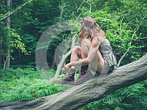 Young woman sitting on fallen tree in forest