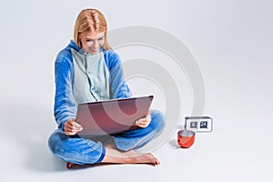Young woman sitting on the floor in his pajamas with a laptop.