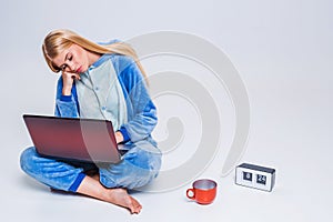 Young woman sitting on the floor in his pajamas with a laptop.