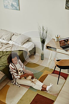 Young woman sitting on floor at home and cuddling with little pet dog