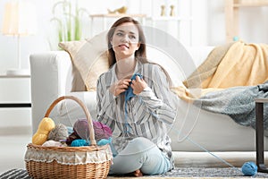 Young woman sitting on floor with knitting clothes at home