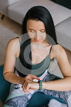 Young woman sitting on the floor and looking at her smartwatch in a cozy house