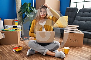 Young woman sitting on the floor at new home using laptop confuse and wonder about question