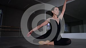 Young woman sitting on floor performing ballet movements lying down. Portrait of skilled Caucasian ballerina rehearsing
