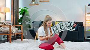 A young woman sitting on the floor of a room, she is dialing numbers on her phone while holding up a thermometer, she
