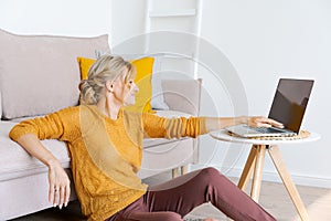 Young woman is sitting on floor by sofa, using laptop. Caucasian woman working